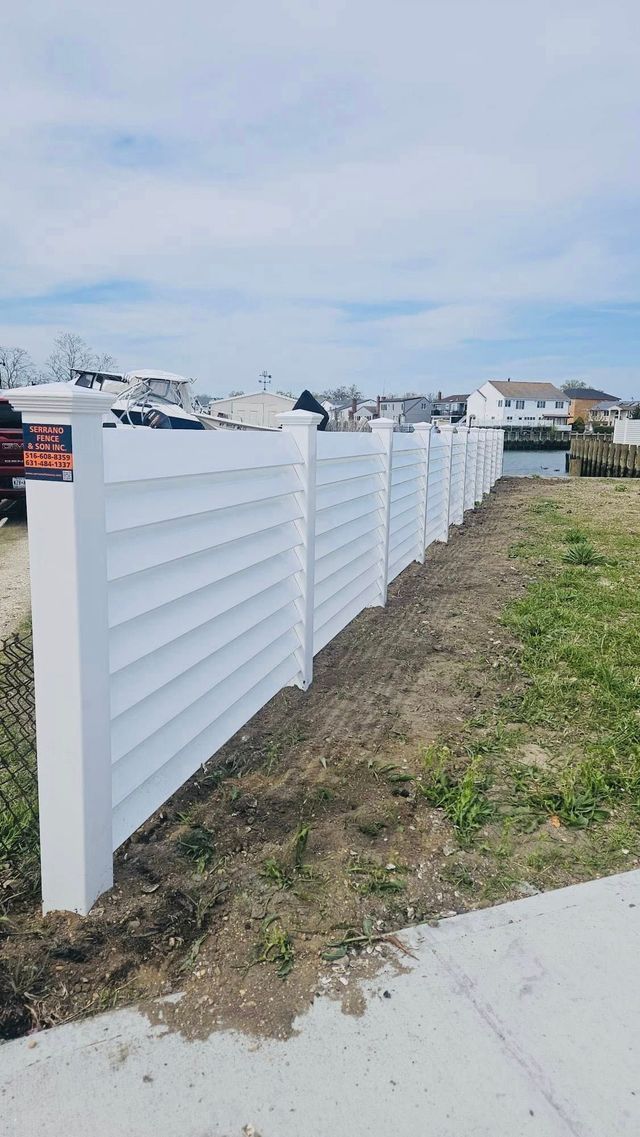 White vinyl fence along a narrow dirt strip beside a sidewalk in a suburban neighborhood