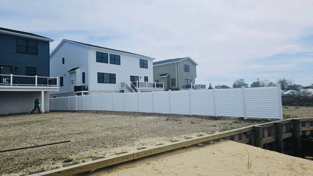 Empty sandy lot beside white and blue houses, fenced off with a deck in the foreground.