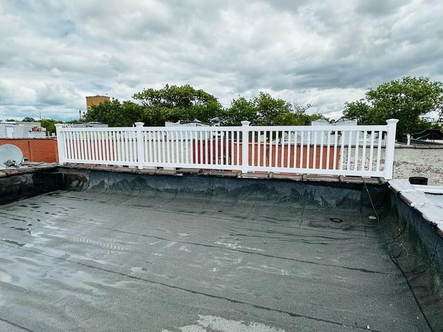 Rooftop terrace with black waterproofing and a white railing under a cloudy sky