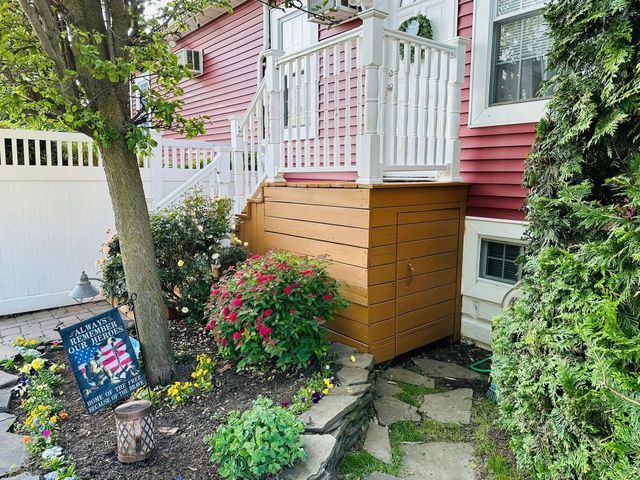 Garden steps beside pink house with white railing, potted flowers, stone path, and white fence