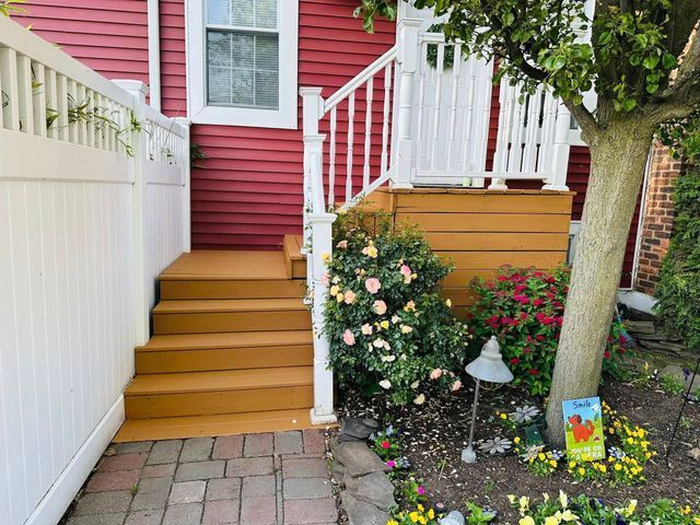 Front steps to a red house beside a white fence, with flowers and a tree-lined garden path