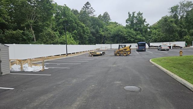 Paved road under construction with barriers, machinery, and trees lining the background
