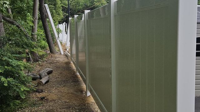 Narrow dirt path beside a tall white fence in a wooded area