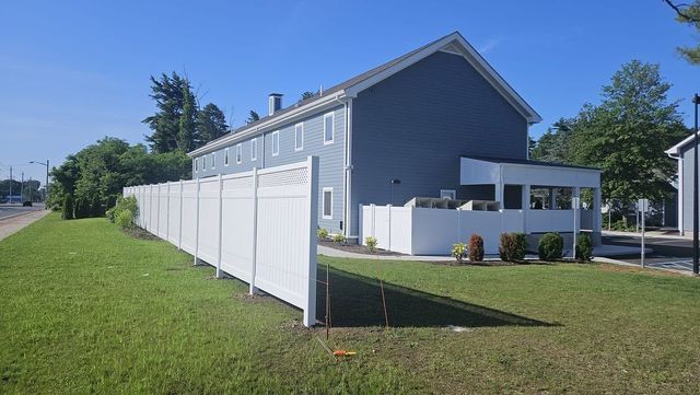 Blue house with white fence beside a grassy lawn under a clear sky.