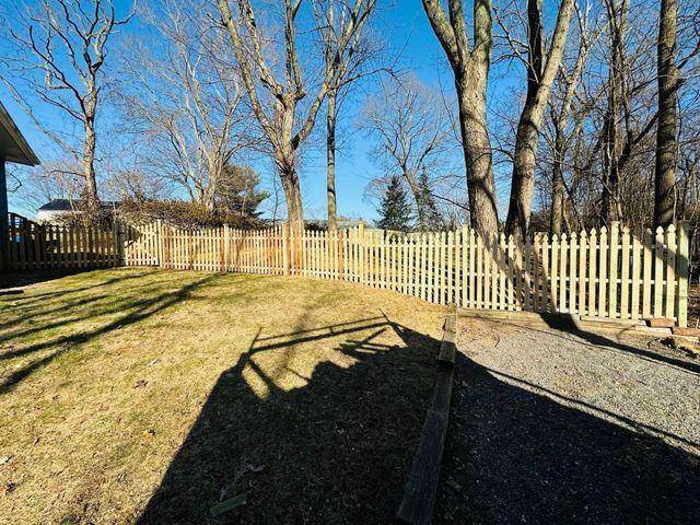 Sunlit backyard with leafless trees, white picket fence, and a shadowed patio in the foreground
