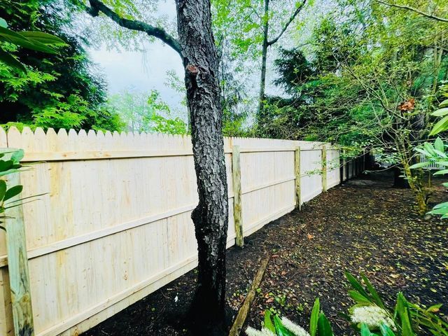 Wooden fence along a tree-lined backyard with green foliage and dark soil ground