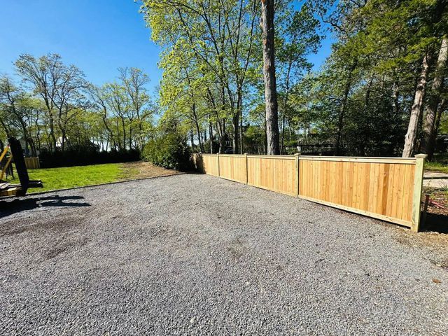 Gravel driveway beside a new wooden fence and trees on a sunny day