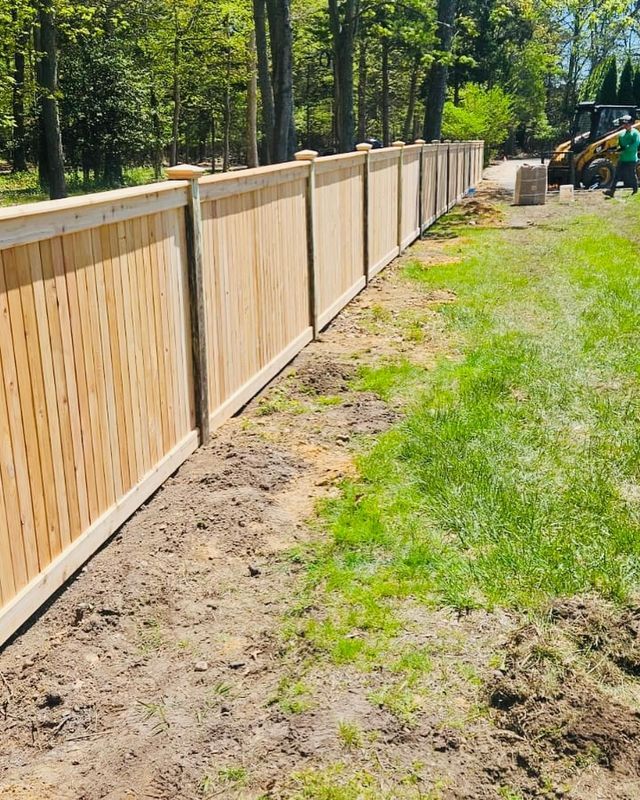 Wooden privacy fence along a grassy yard beside trees, with construction equipment in the distance.