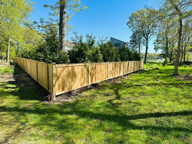 Wooden fenced garden plot in a grassy park with trees and blue sky.