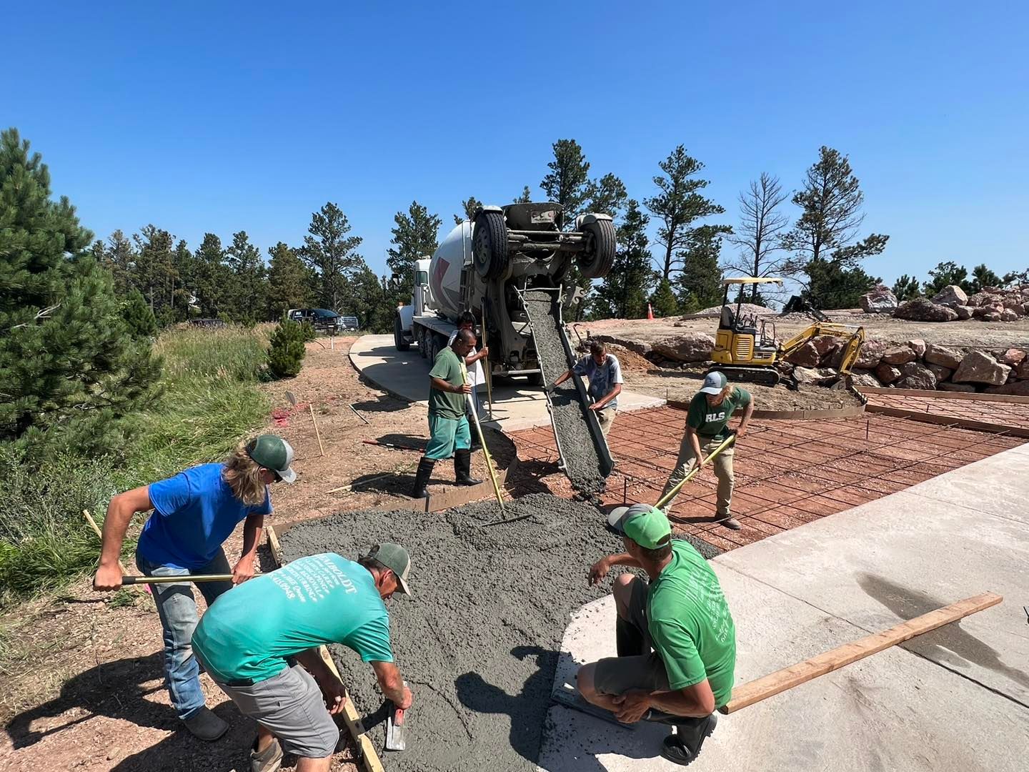 Workers spread wet concrete from a truck chute onto a stone-covered base during an outdoor construction project.
