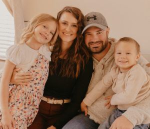 A smiling family of four posing together in a bright, indoor setting.