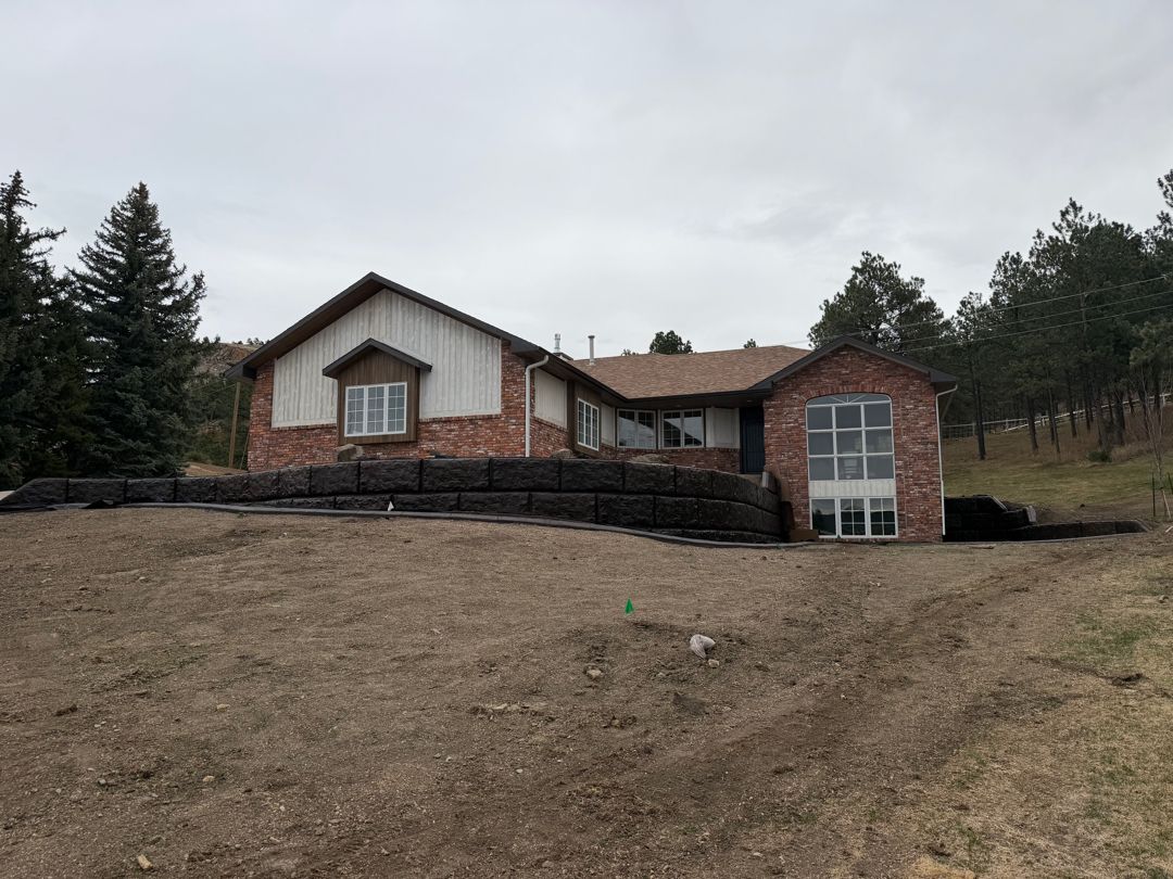Red-brick house with white siding on a grassy hillside under a cloudy sky