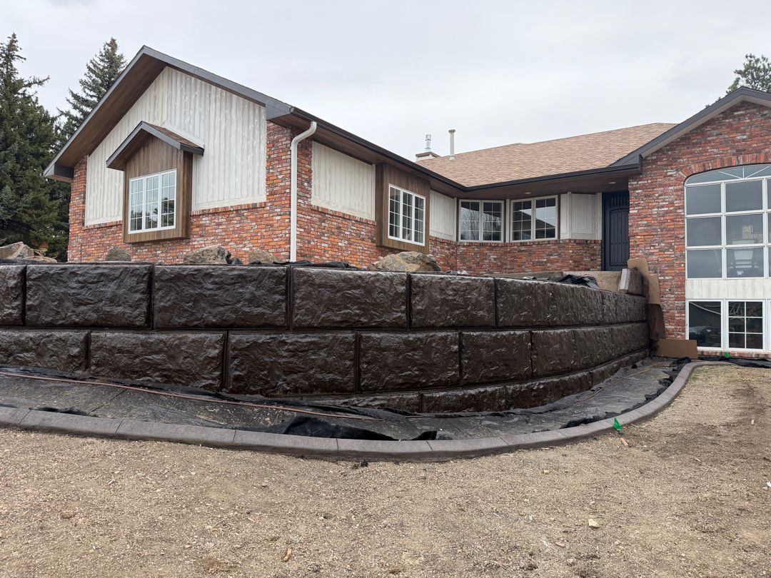 Brick house with tall retaining wall and unfinished gravel yard under a cloudy sky