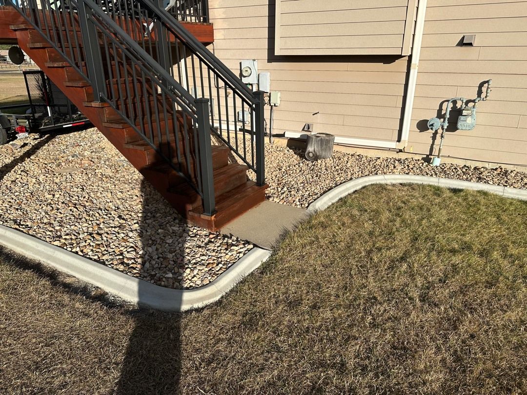 Front steps with black railing beside a tan house, bordered by a rock bed and winter grass.