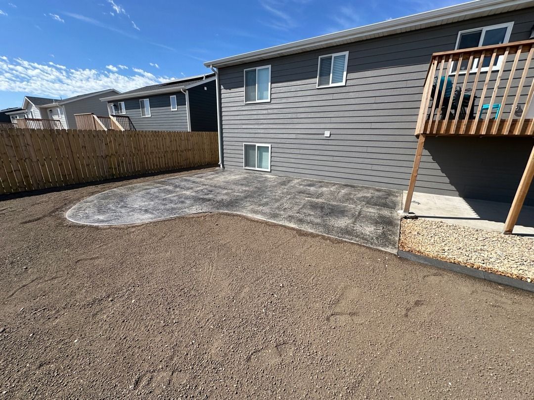 Backyard with gravel ground, gray house siding, wooden deck, and fenced yard under a clear sky
