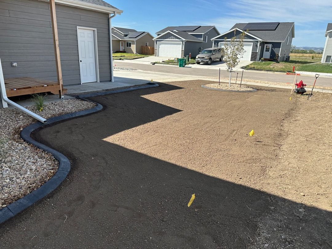 Newly landscaped backyard with gravel border, dirt lawn, and a house exterior on the left.