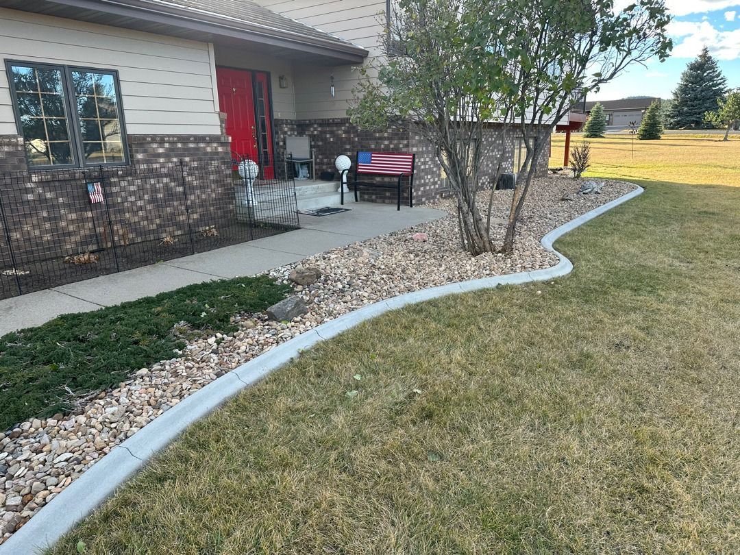 Front yard with house, red door, curved stone border, shrubs, and dry grass lawn.