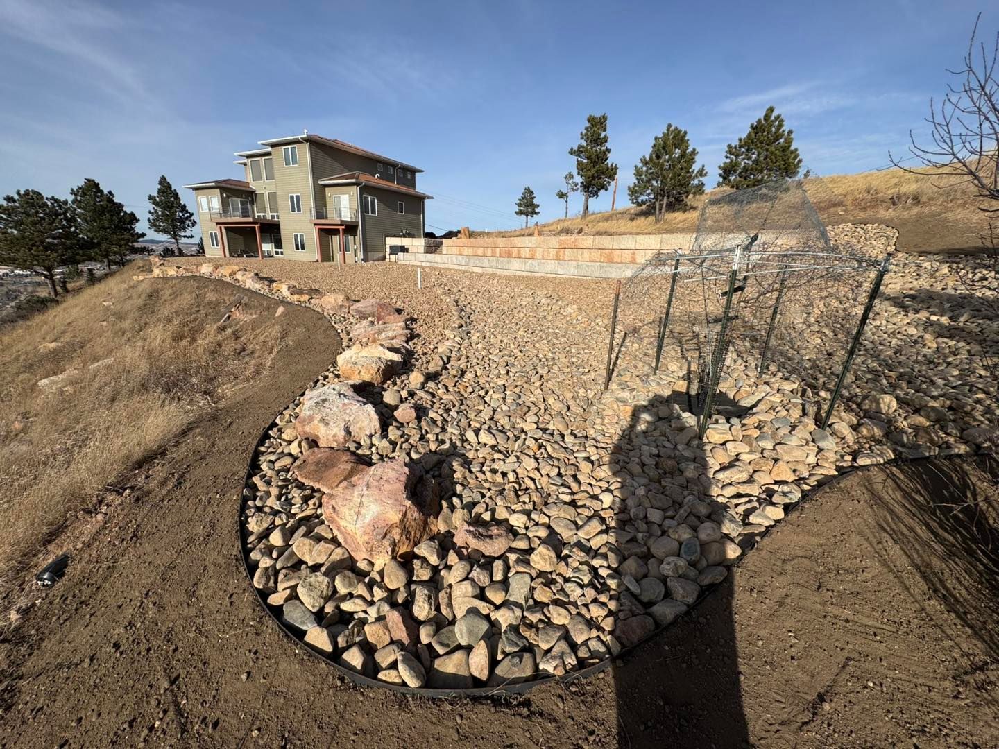 House on a hillside with a stone retaining wall and newly landscaped slope under a blue sky
