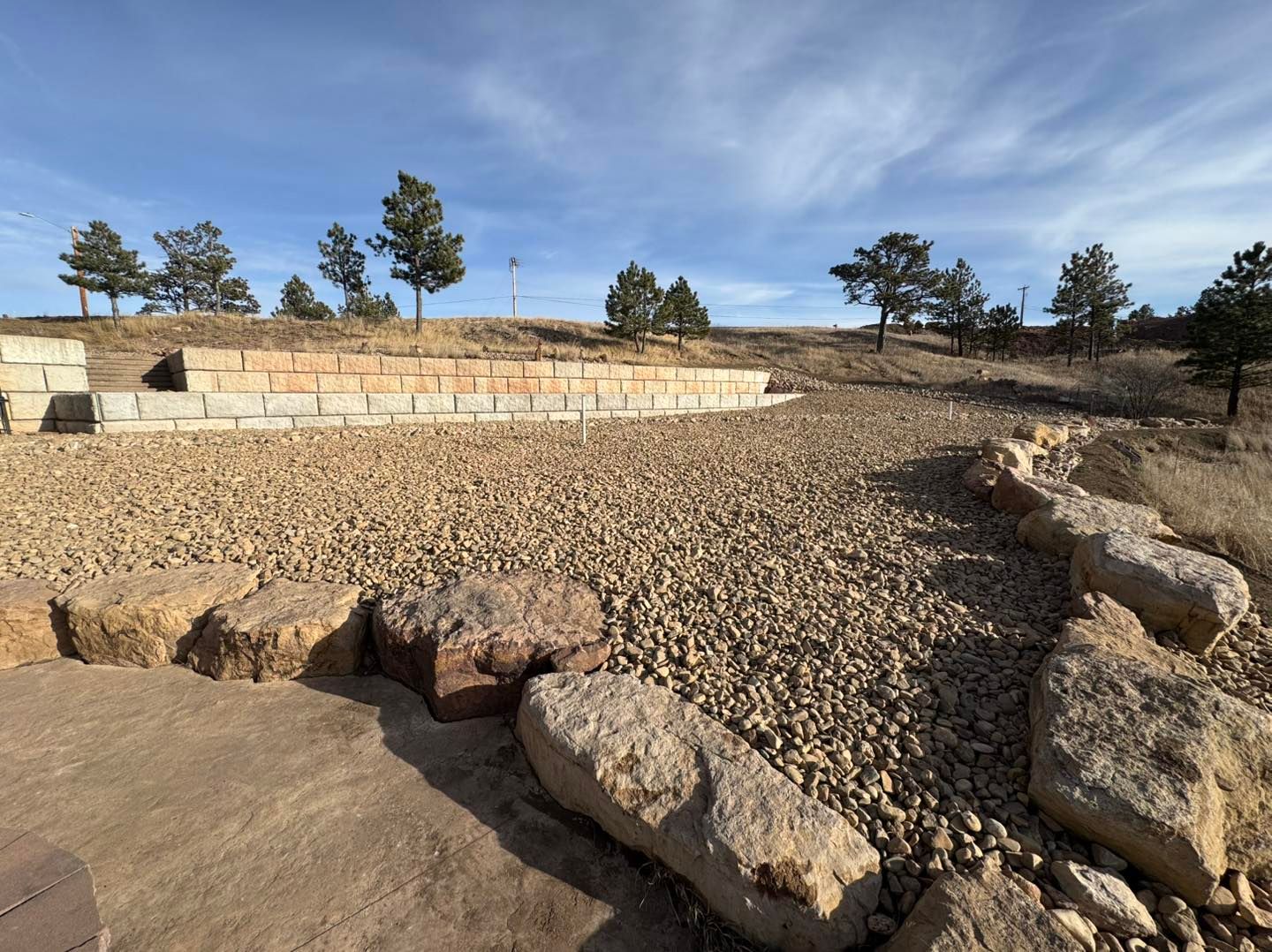 Rocky terraced landscape with stone retaining walls and sparse trees under a clear blue sky