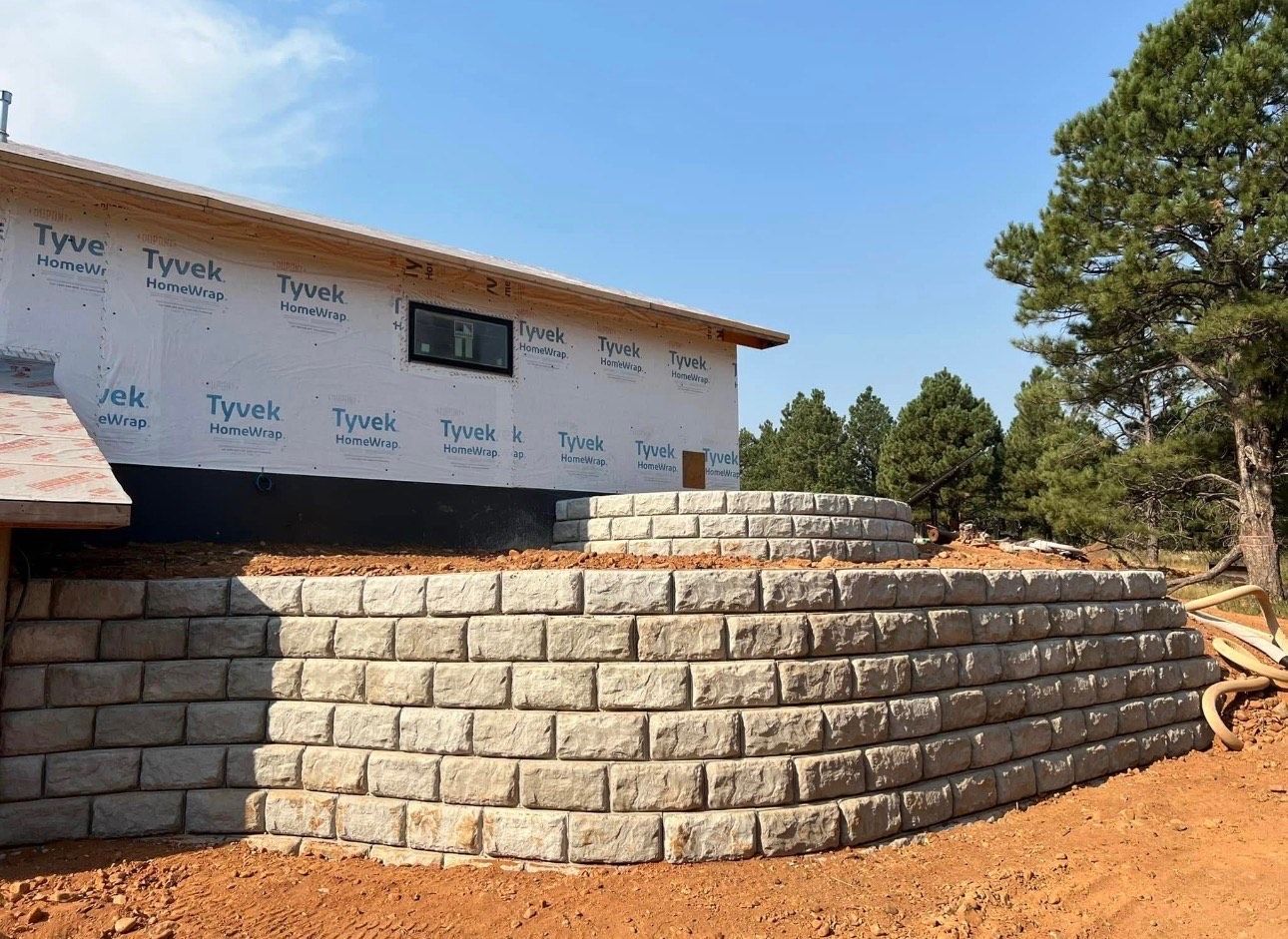 Stone retaining wall under construction beside a house on a dirt lot