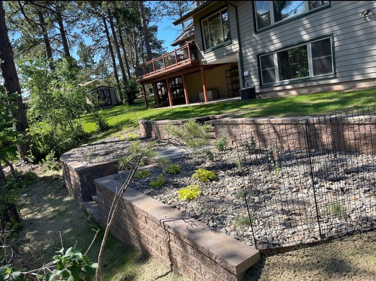 Sloped landscaped front yard with stone retaining wall, gravel beds, and a house with covered porch.