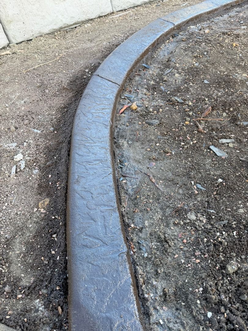 Curved gray concrete curb edging a dirt path beside a wall