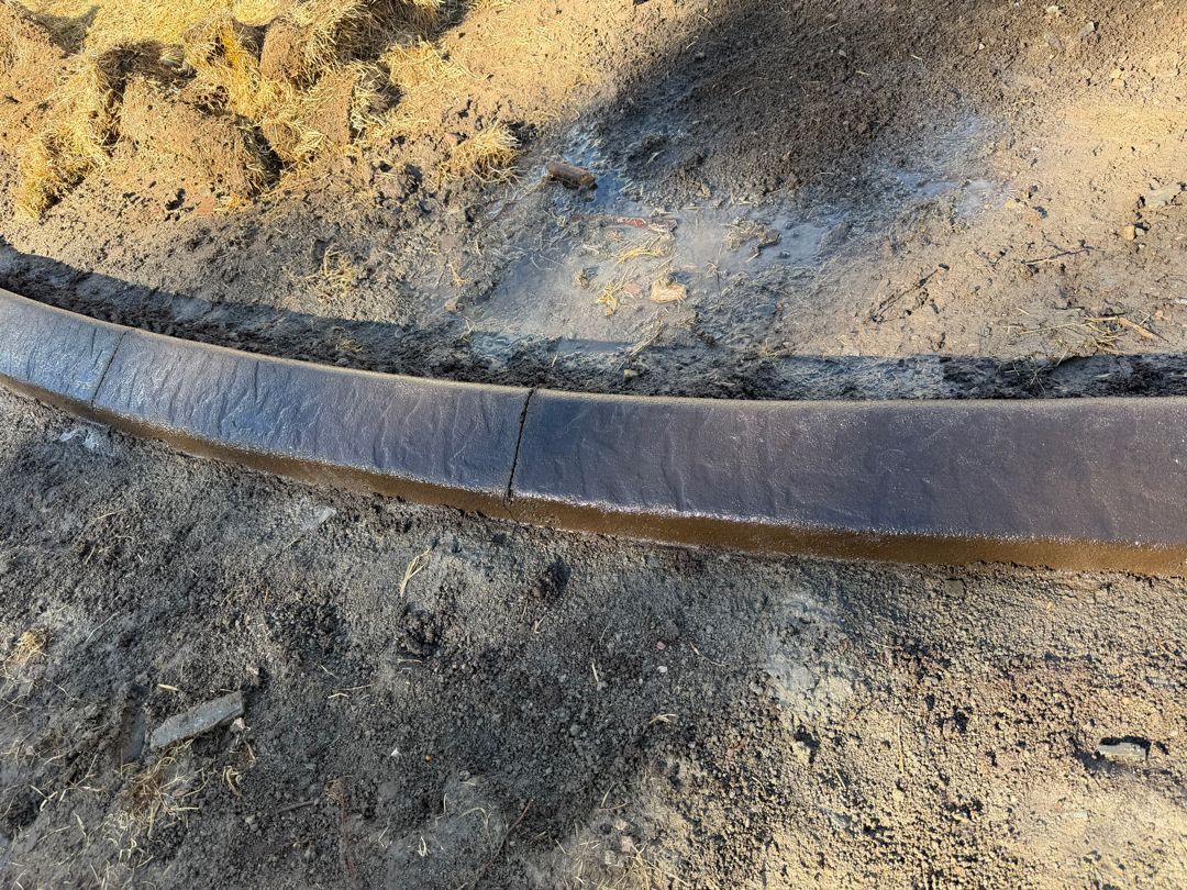 Curved gray metal strip embedded in dirt and gravel outdoors