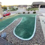 A green, U-shaped patch of hydroseeded grass bordered by rocks, situated in a residential yard near a parked red car.