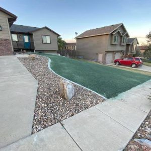 A house exterior featuring a front yard with a smooth green lawn, gravel border, concrete walkway, and a red car parked.