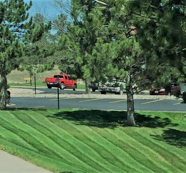 A red truck parked in a sunny parking lot near a grassy slope with distinct, diagonal lawn-mower stripes.
