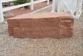 A large red stone block is sitting on the ground in front of a white fence.
