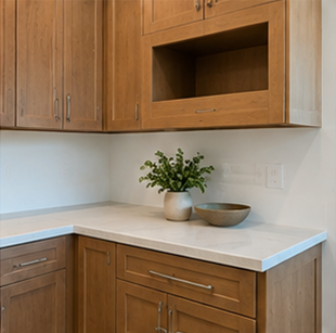 Wooden kitchen cabinets with white countertop, potted plant, bowl, and built-in shelf niche