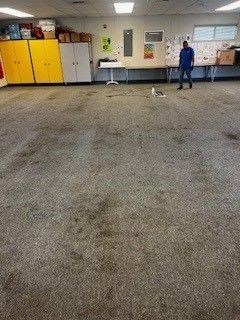 A man is standing on a dirty carpeted floor in a room.