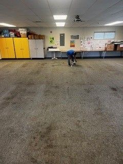 A person is kneeling on a dirty carpet in a room.
