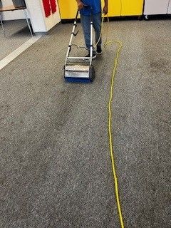 A man is cleaning a carpet with a vacuum cleaner.