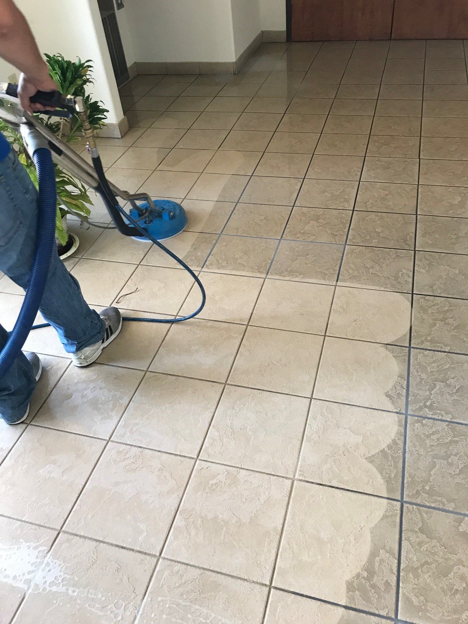 A person is cleaning a tile floor with a vacuum cleaner.