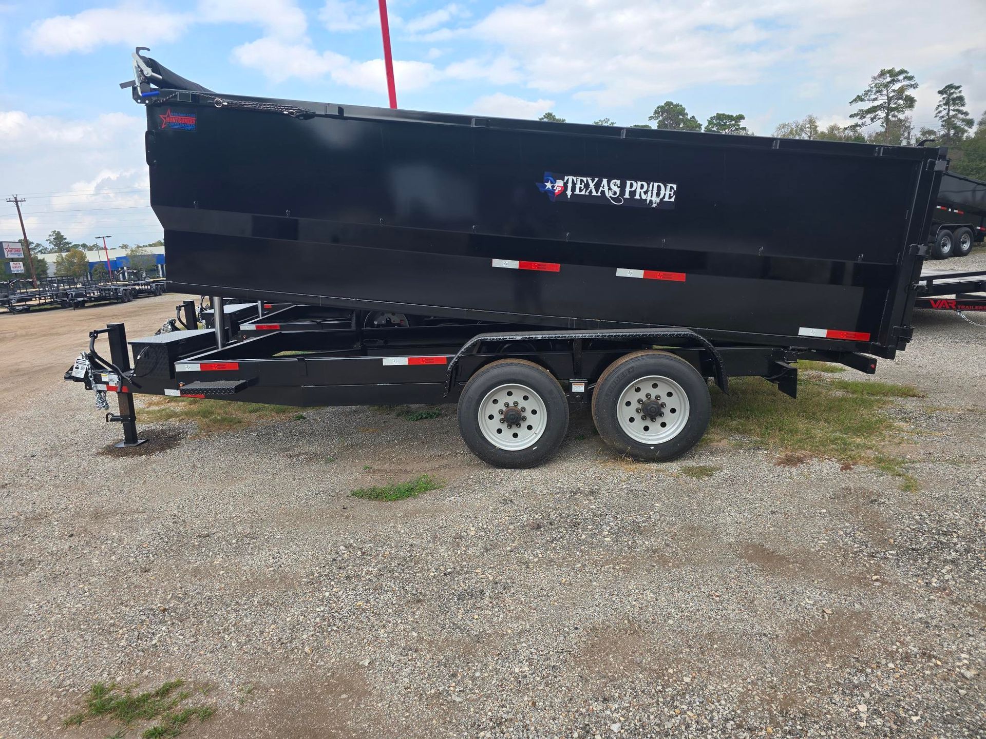 Black dump trailer with two wheels on gravel.