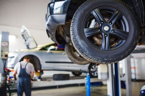 Car lifted in auto shop with mechanic working underneath and a tire in the foreground