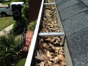 A residential rain gutter filled with a large amount of dried autumn leaves, seen from above near a roof edge.