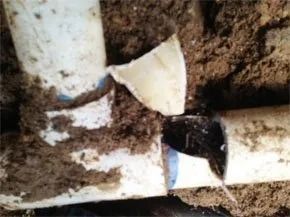 A broken white PVC plumbing T-joint pipe covered in soil.