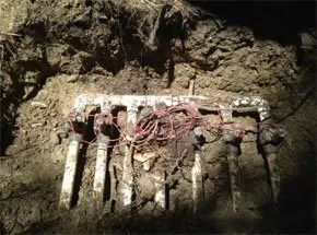 An underground irrigation valve manifold with several valves and a tangled bundle of red wiring, set in a dirt trench.