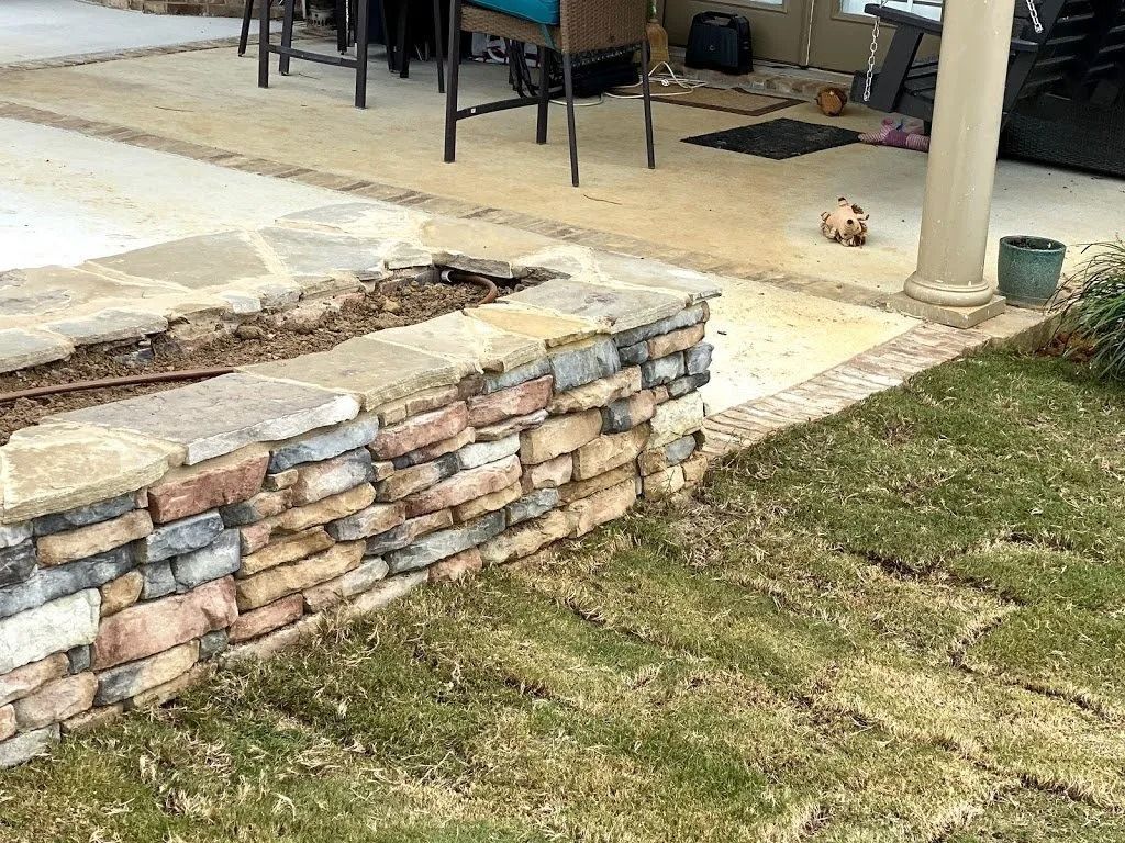 A stone retaining wall bordering a patio and a newly laid sod lawn.