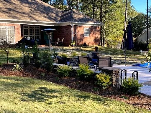 A red brick house with a backyard patio featuring outdoor furniture, a fire pit, and a dark blue umbrella on a sunny day.