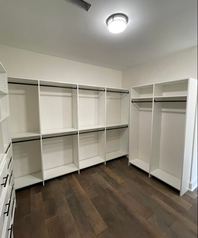 a walk in closet with white shelves and wooden floors
