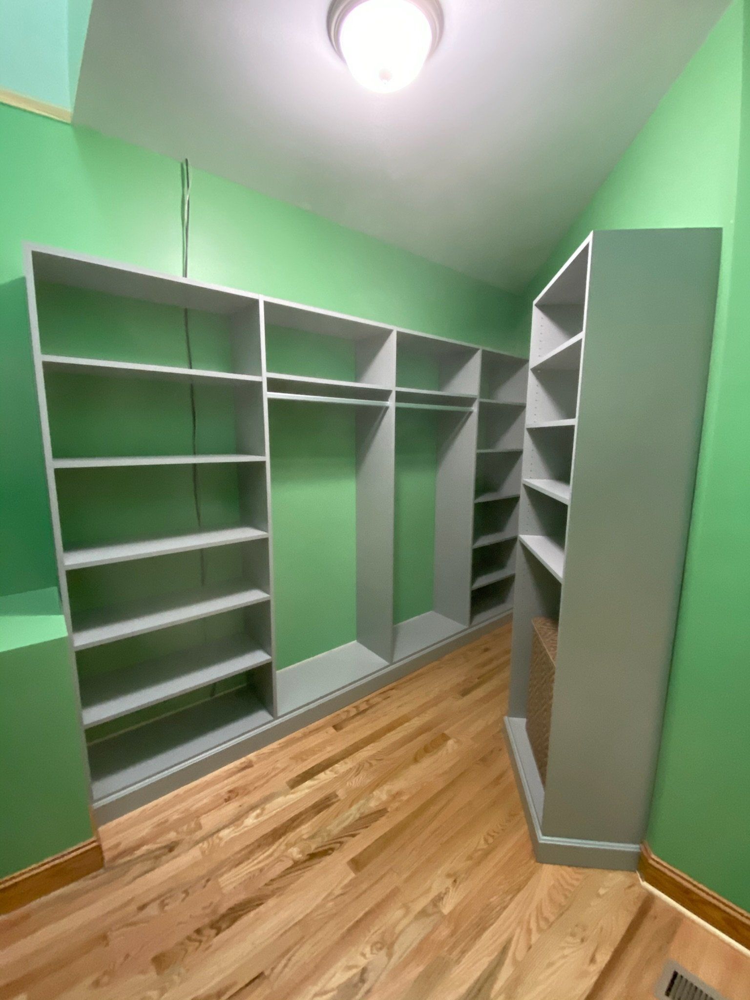 a walk in closet with green walls and wooden floors
