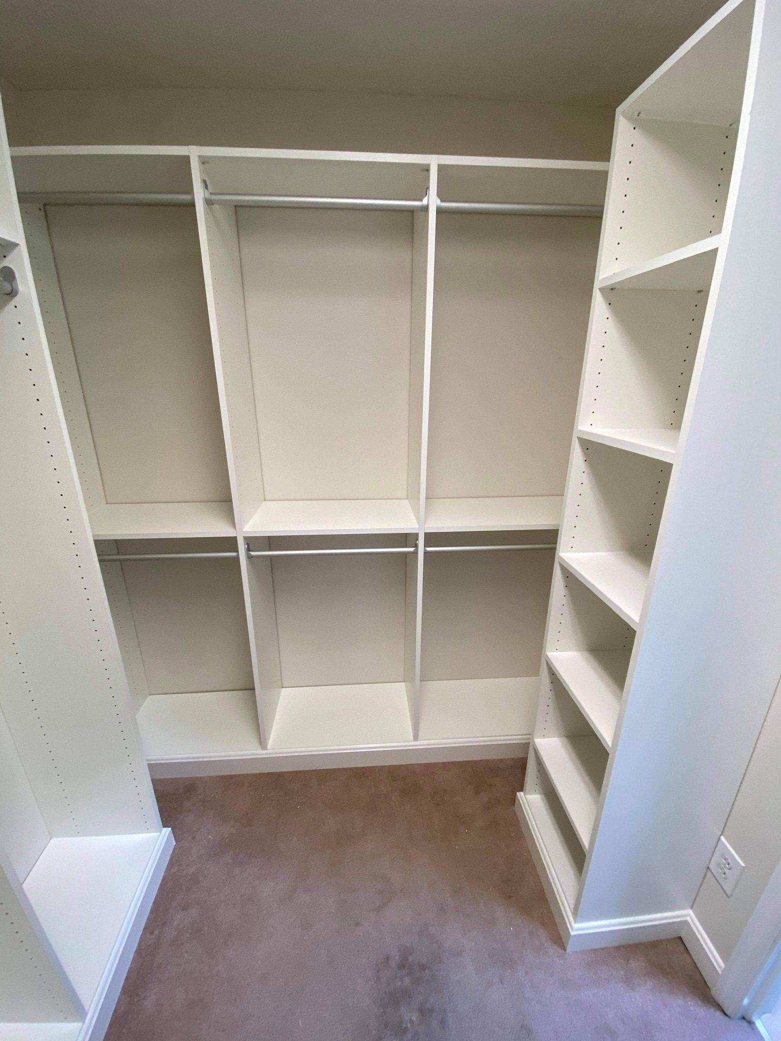 a walk in closet with white shelves and clothes racks