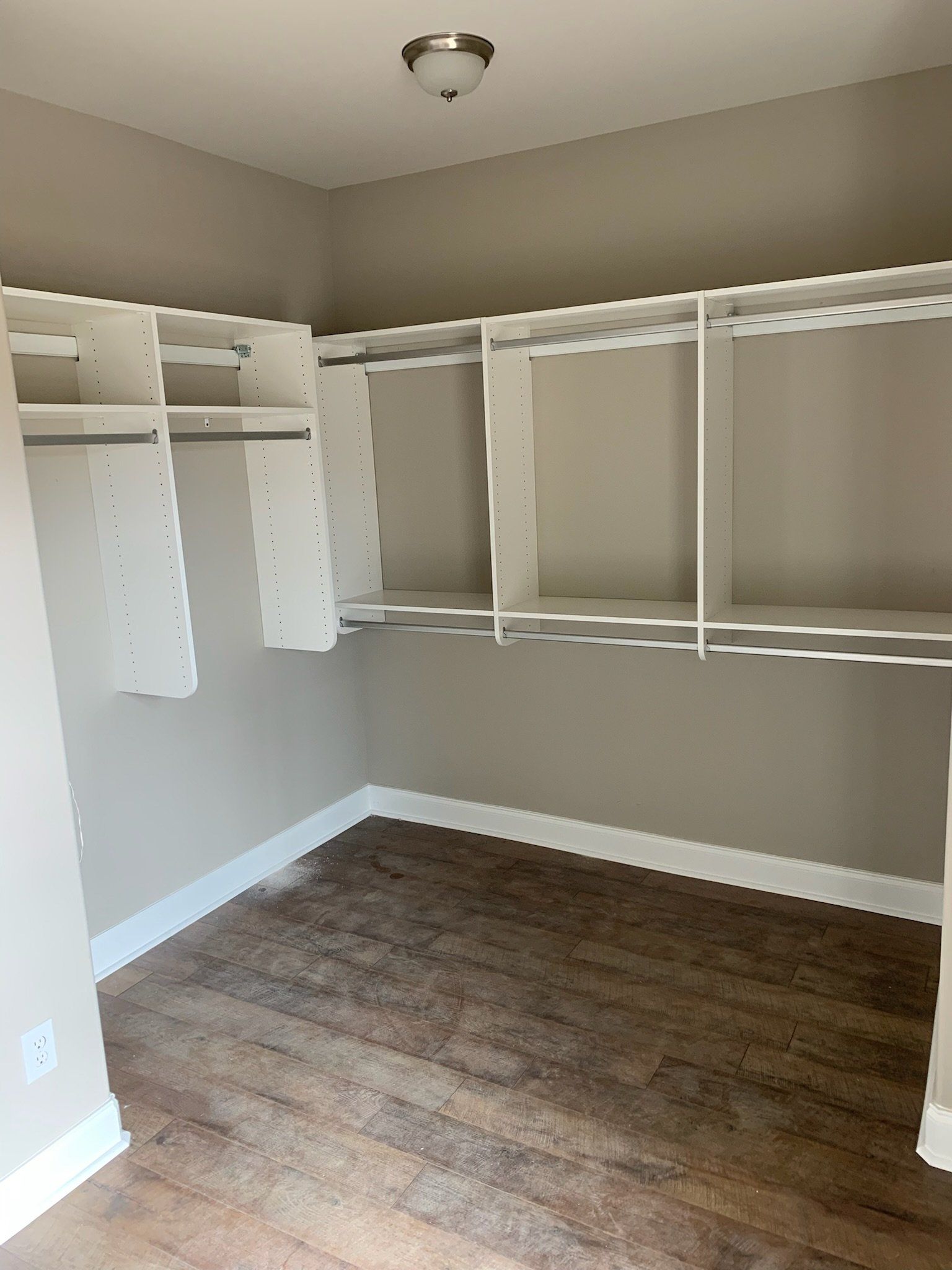an empty walk in closet with wooden floors and white shelves