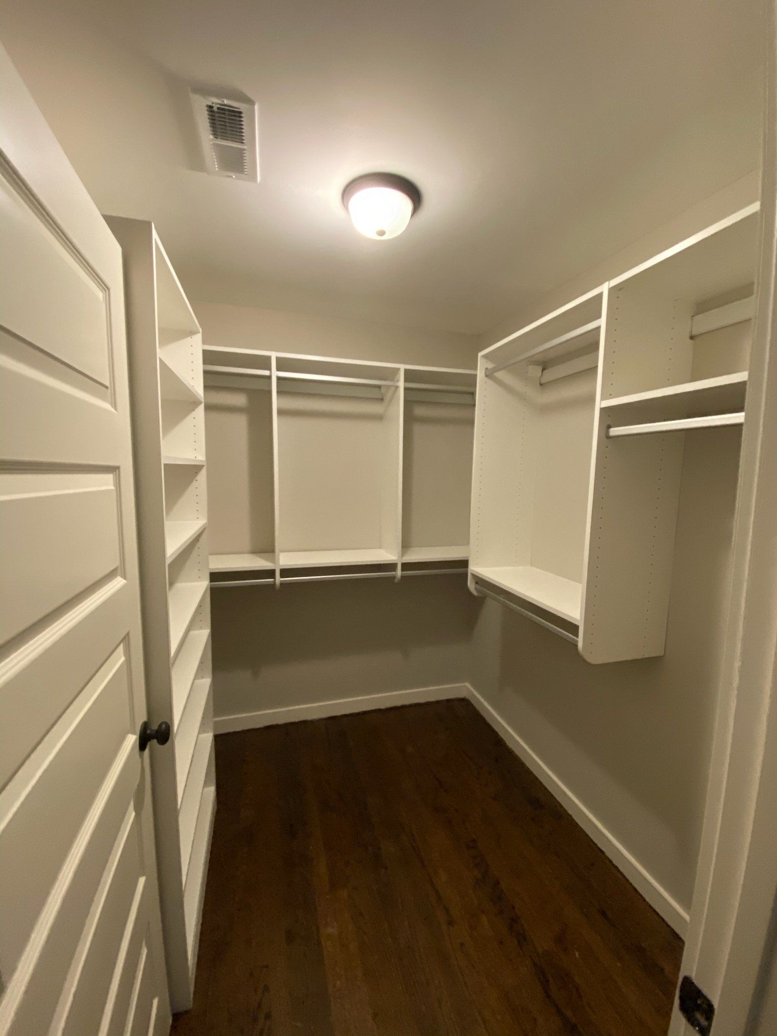 a walk in closet with white shelves and wooden floors