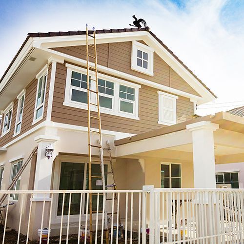 A man is painting the roof of a house with a ladder