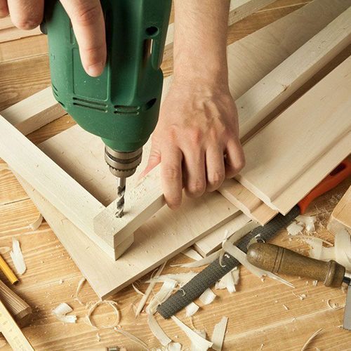 A person is using a green drill on a piece of wood
